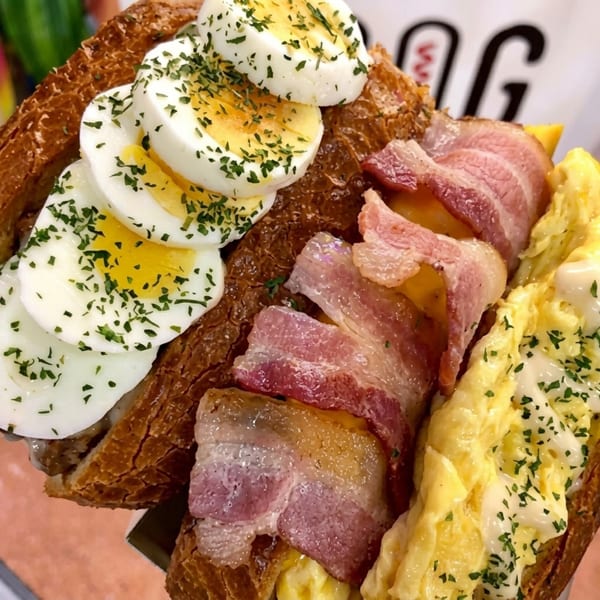 Oh-K Dog Egg Toast with sliced hard-boiled eggs, bacon, and scrambled eggs on a toasted bun.