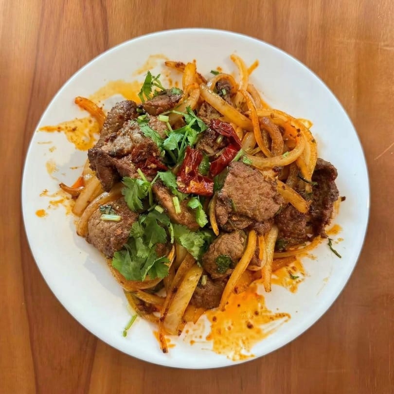 Korean stir-fried beef with onions, red peppers, and cilantro on a white plate.
