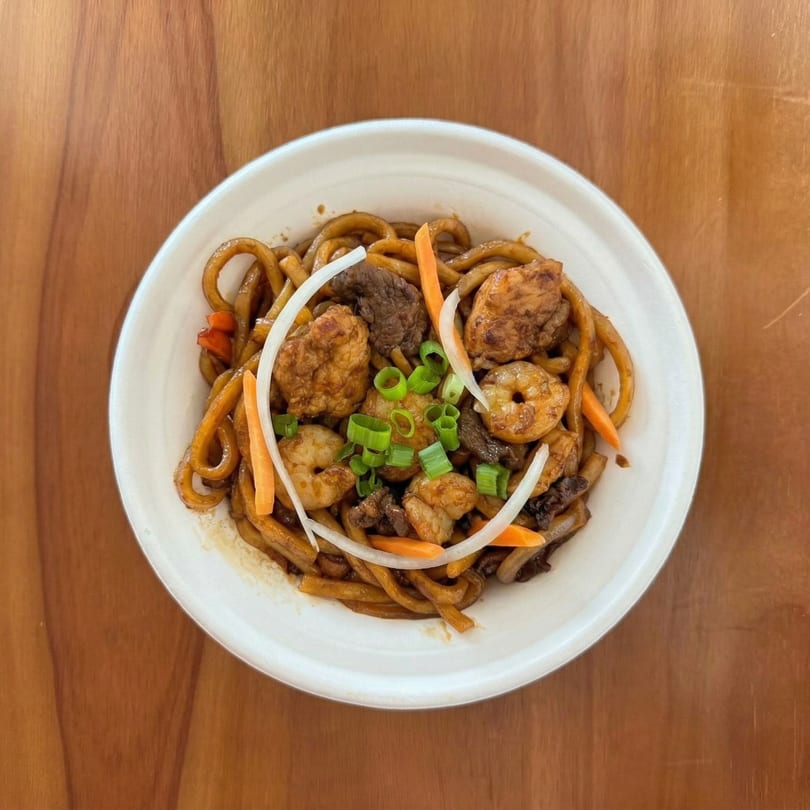 Korean noodles with beef, shrimp, carrots, onions, and green onions in a white bowl.