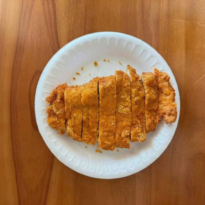 Crispy, golden-brown Korean fried chicken cutlets, sliced and served on a white paper plate.